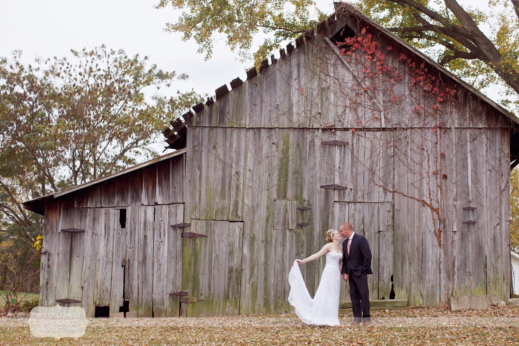 bride and groom stand outside of an old barn in rocheport, mo for their fall wedding