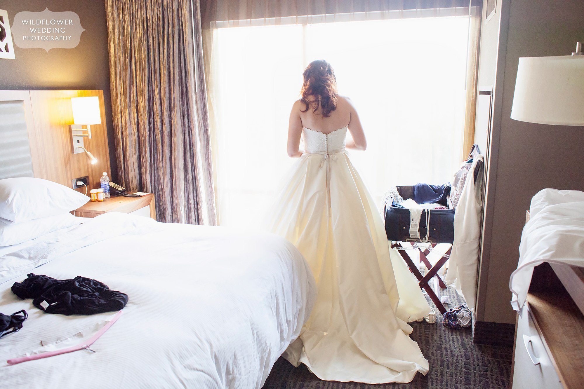 Natural wedding photo of the bride looking out a large window of the Broadway Hotel in Columbia, MO.