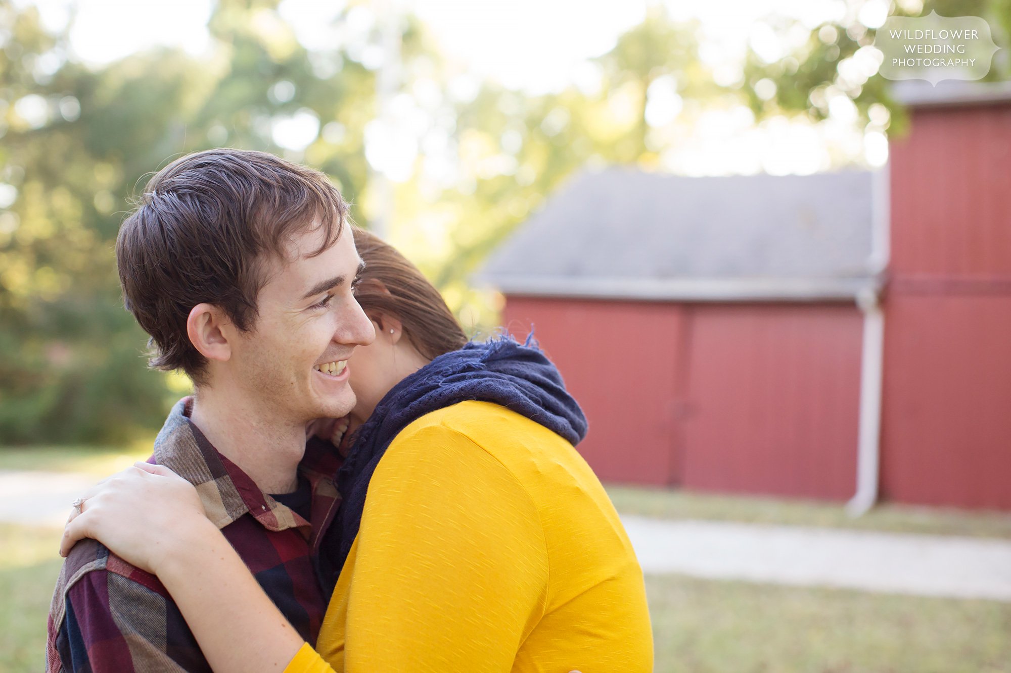 Engagement photo of couple hugging in front of a red barn in October in Columbia, MO.