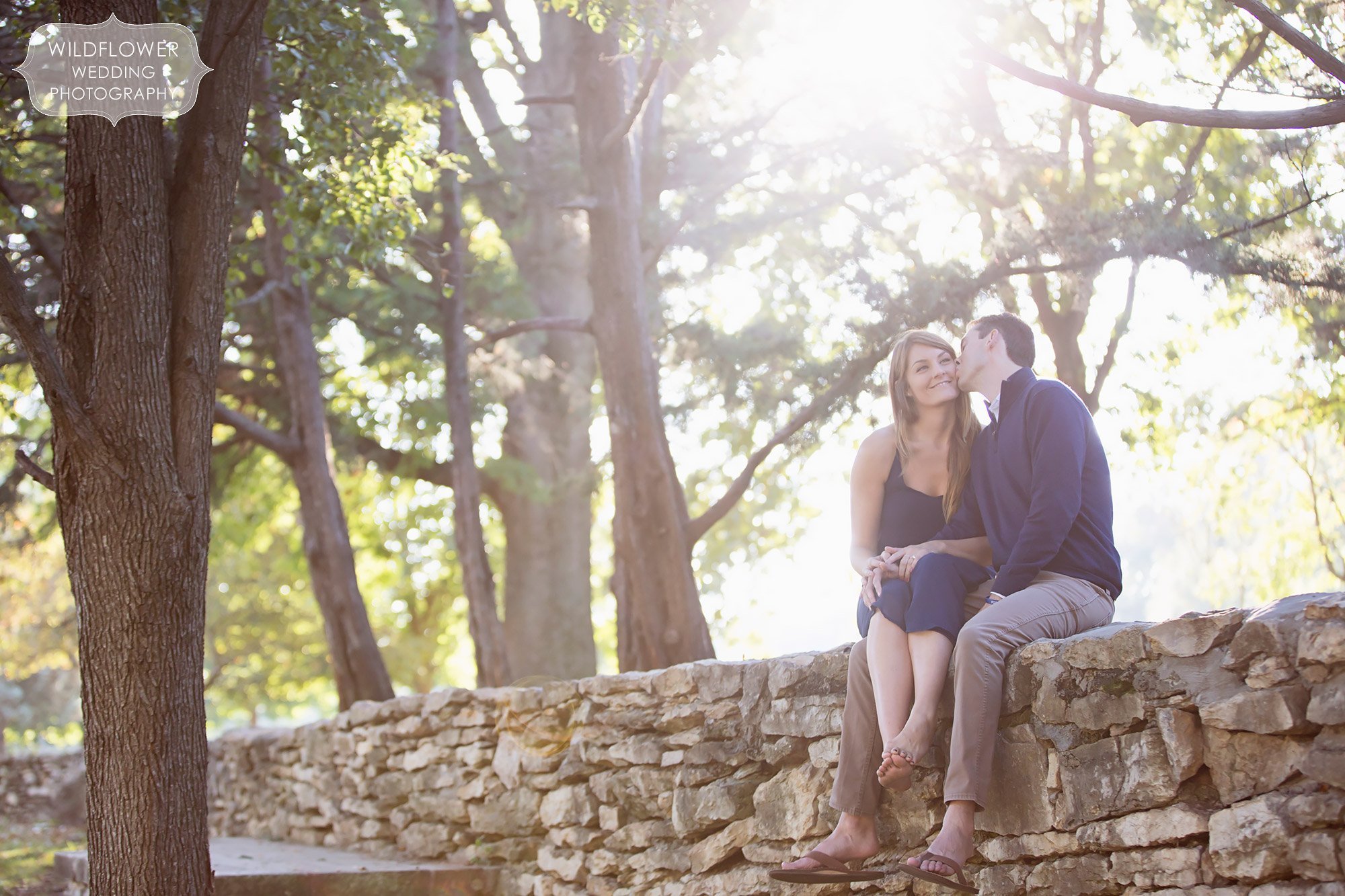 Engagement photo of the couple sitting up on a rock wall kissing at Loose Park in KC, MO.