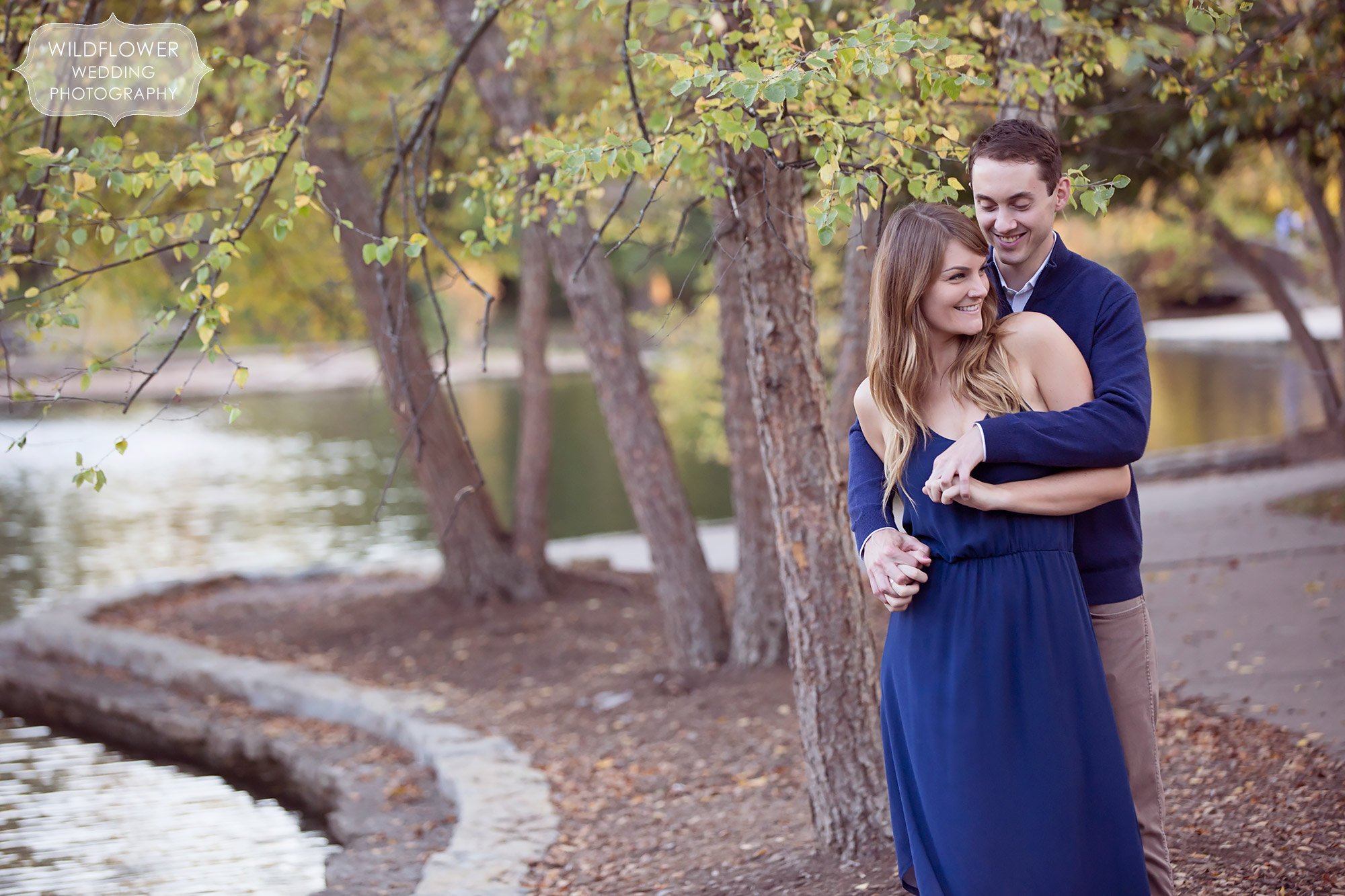 Couple embracing next to a pond with a navy dress and dark sweater at Loose Park in KC, MO.