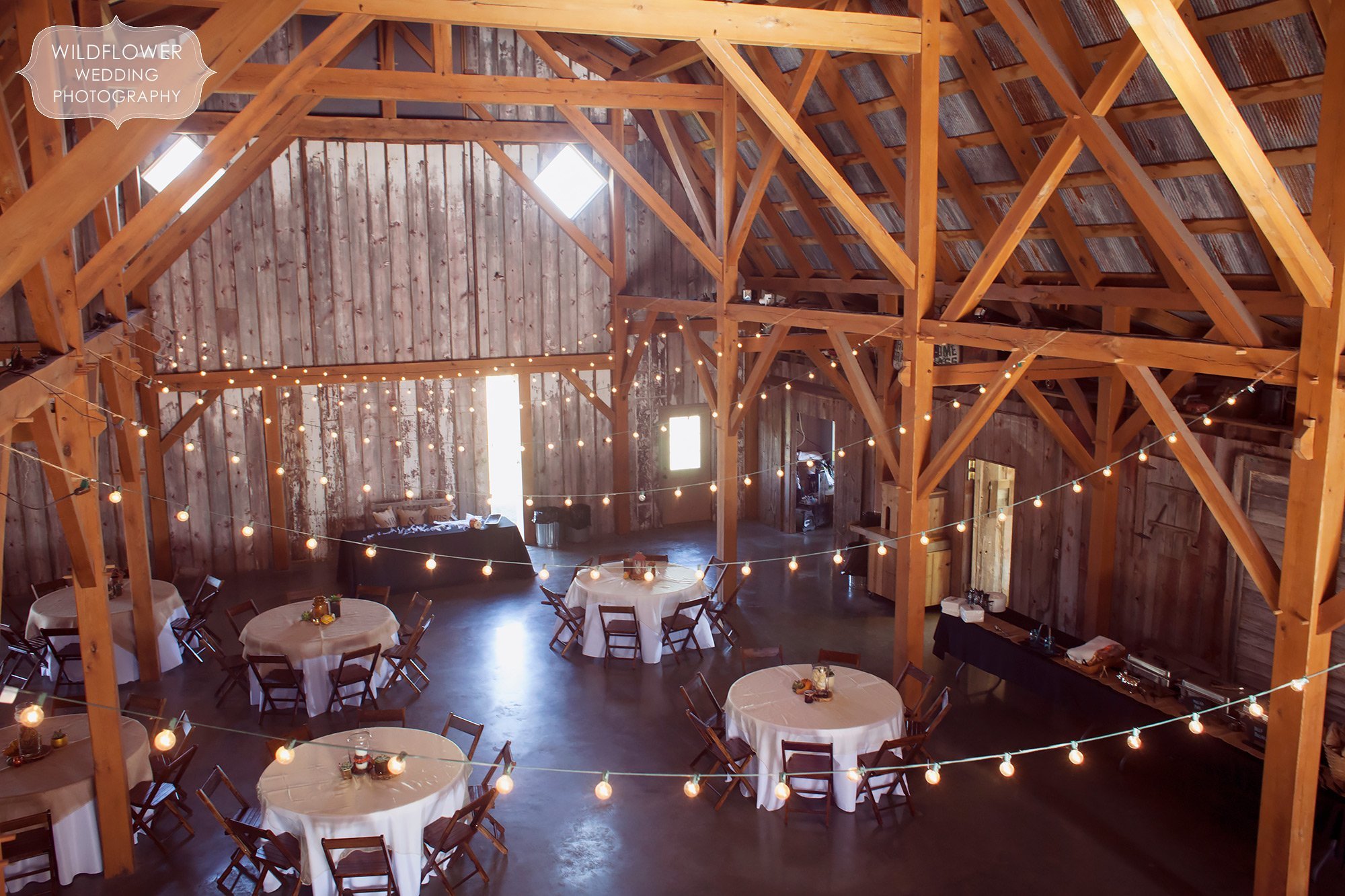 View of the inside of the timber frame barn at the Schwinn Produce Farm with dinner tables set up and cafe string lights above.