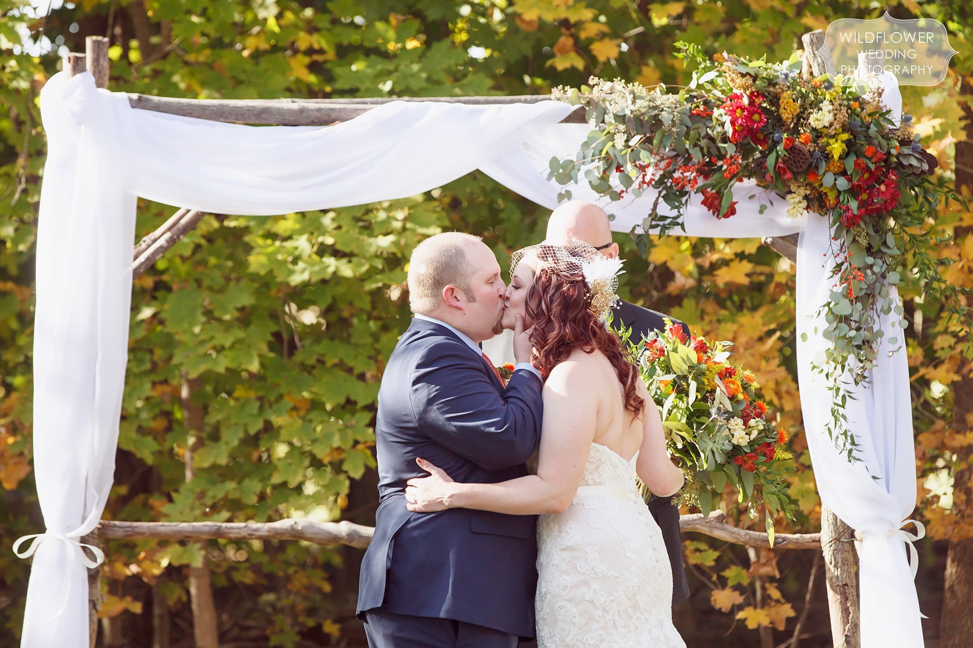 The bride and groom share their first kiss at the end of their outdoor ceremony at the Schwinn Produce Farm venue.