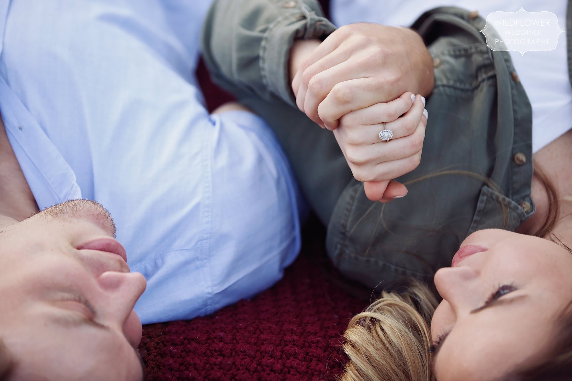 Engagement photo detail picture of couple holding hands with rings while laying on a blanket in Columbia, MO.