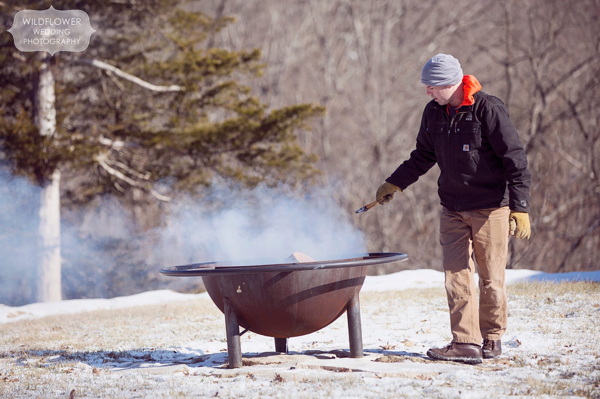 The owner of the property tends to the fire pit for this same-sex winter wedding in Columbia, MO.