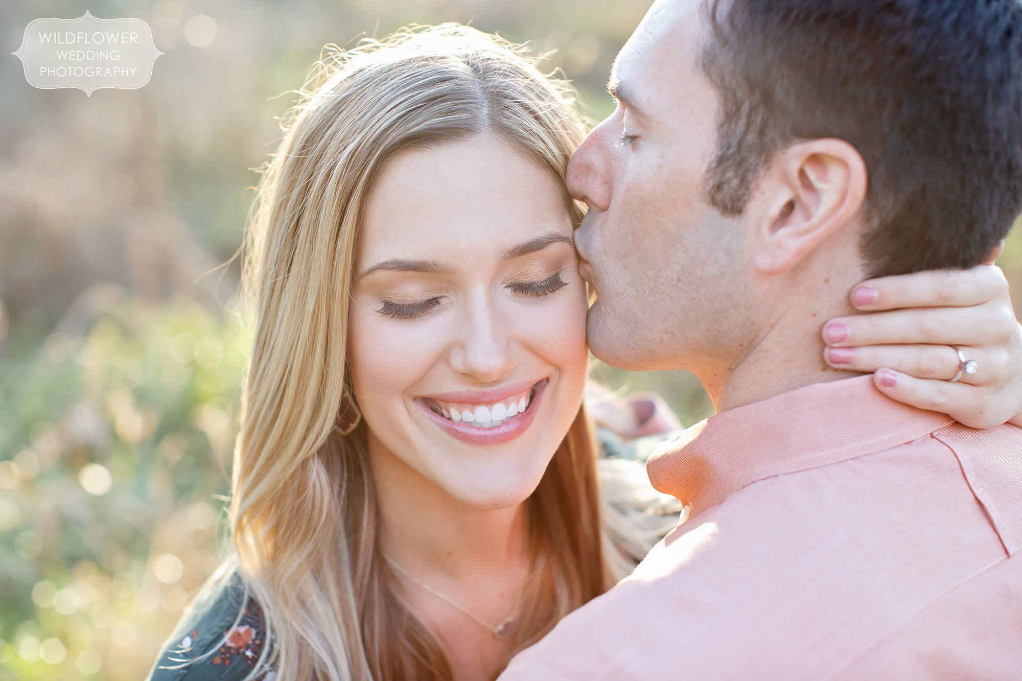 Anthropologie engagement photography pose with guy kissing girl on the cheek in sunbursty light at Grindstone Park.