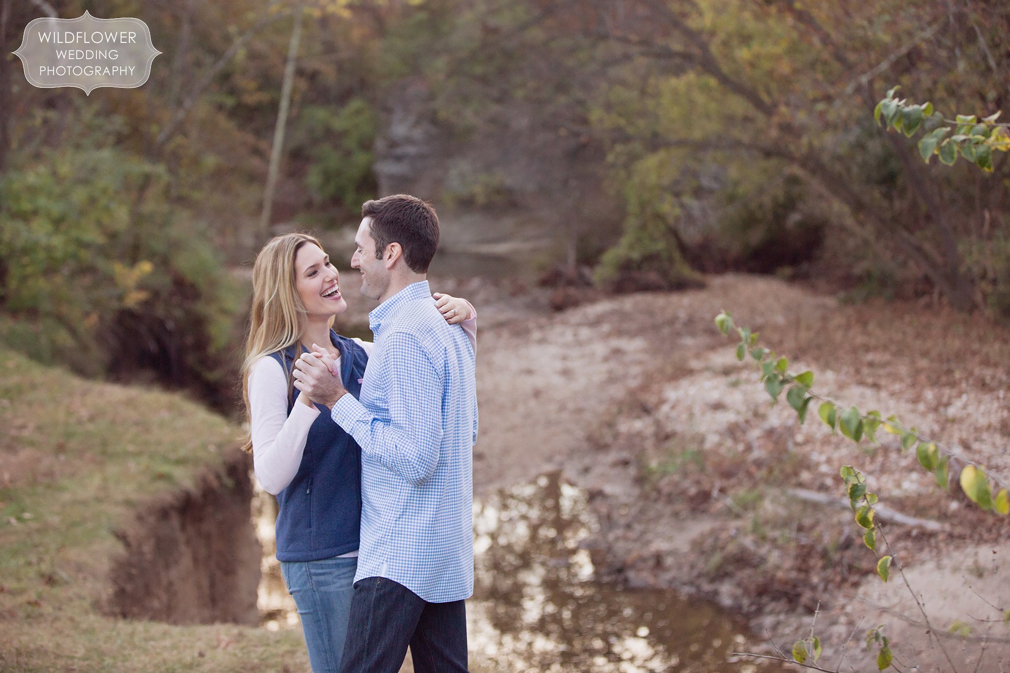 Sweet candid engagement photo of the couple laughing next to the Hinkson Creek during their outdoor Anthropologie engagement photography session.