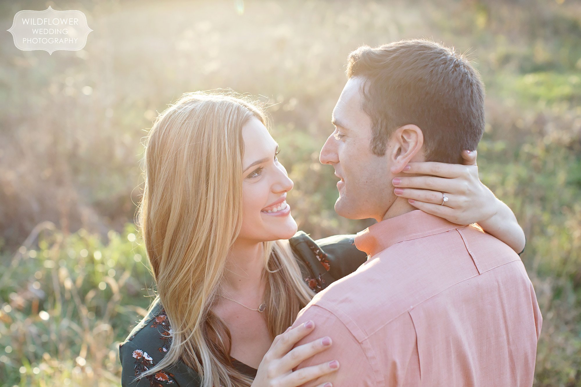 Candid engagement photo of the couple smiling at each other in the sunset in a field at Grindstone.