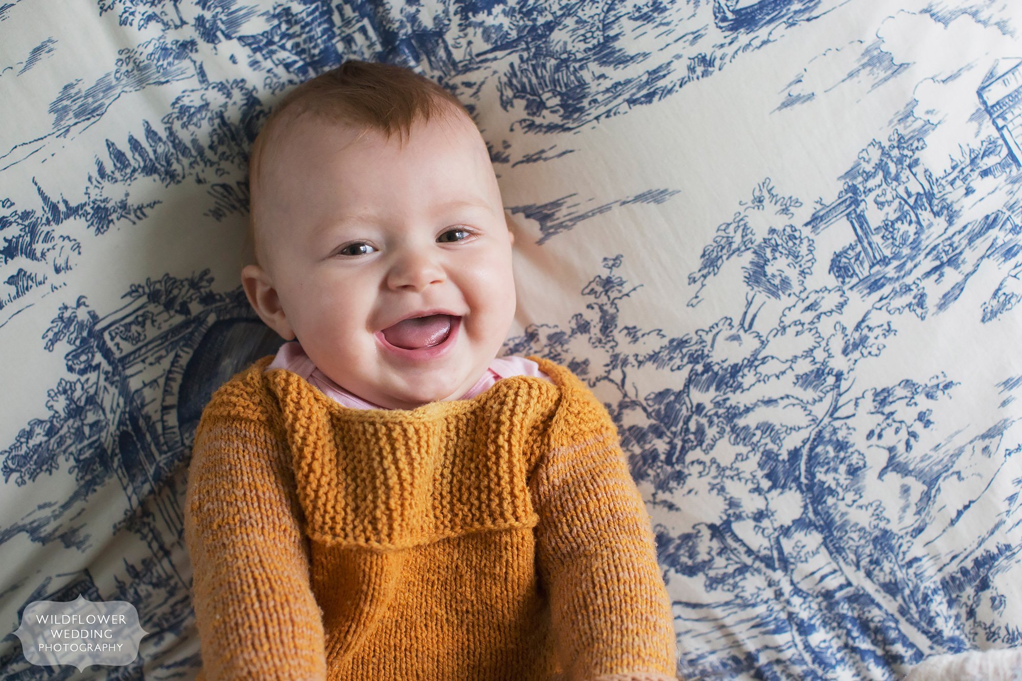 Laughing eight month old baby in handmade orange sweater by Wool Crush during a documentary photo shoot.