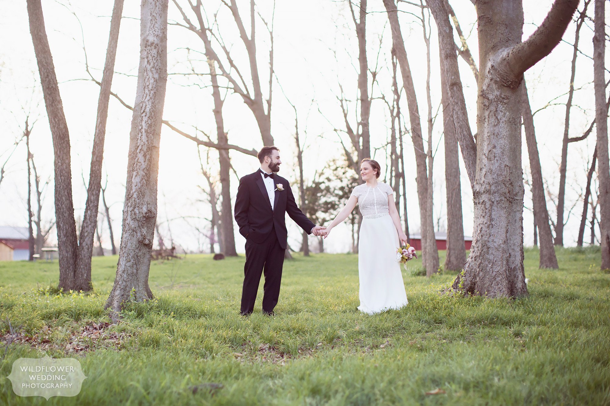 Bride and groom hold hands under the trees at Nifong Park after their rustic elopement at the gazebo.