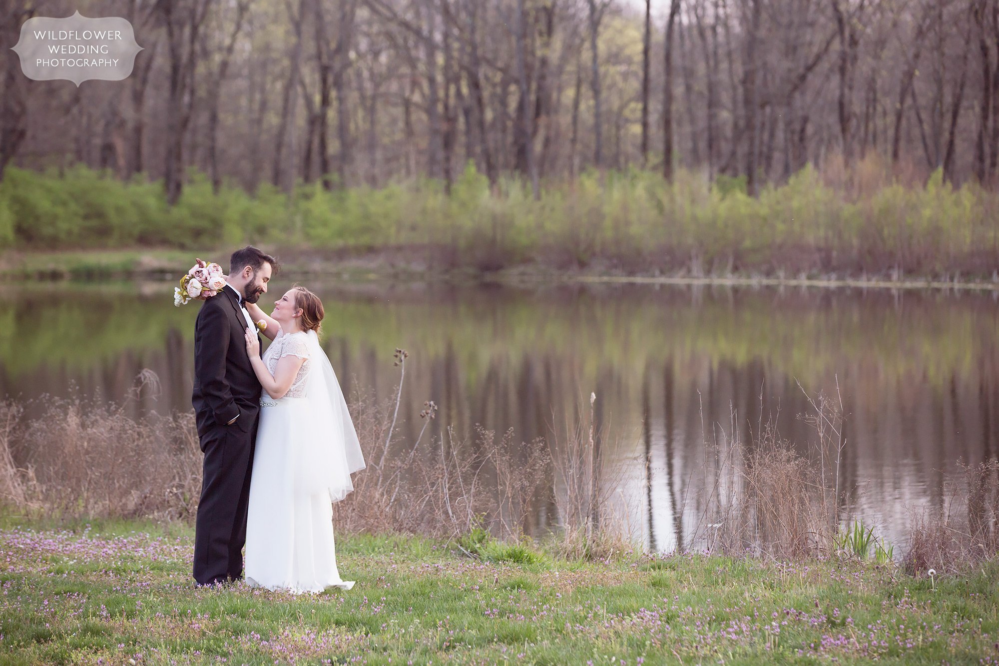 Bride and groom pose next to a pond during their lakeside elopement venue at Nifong Park.