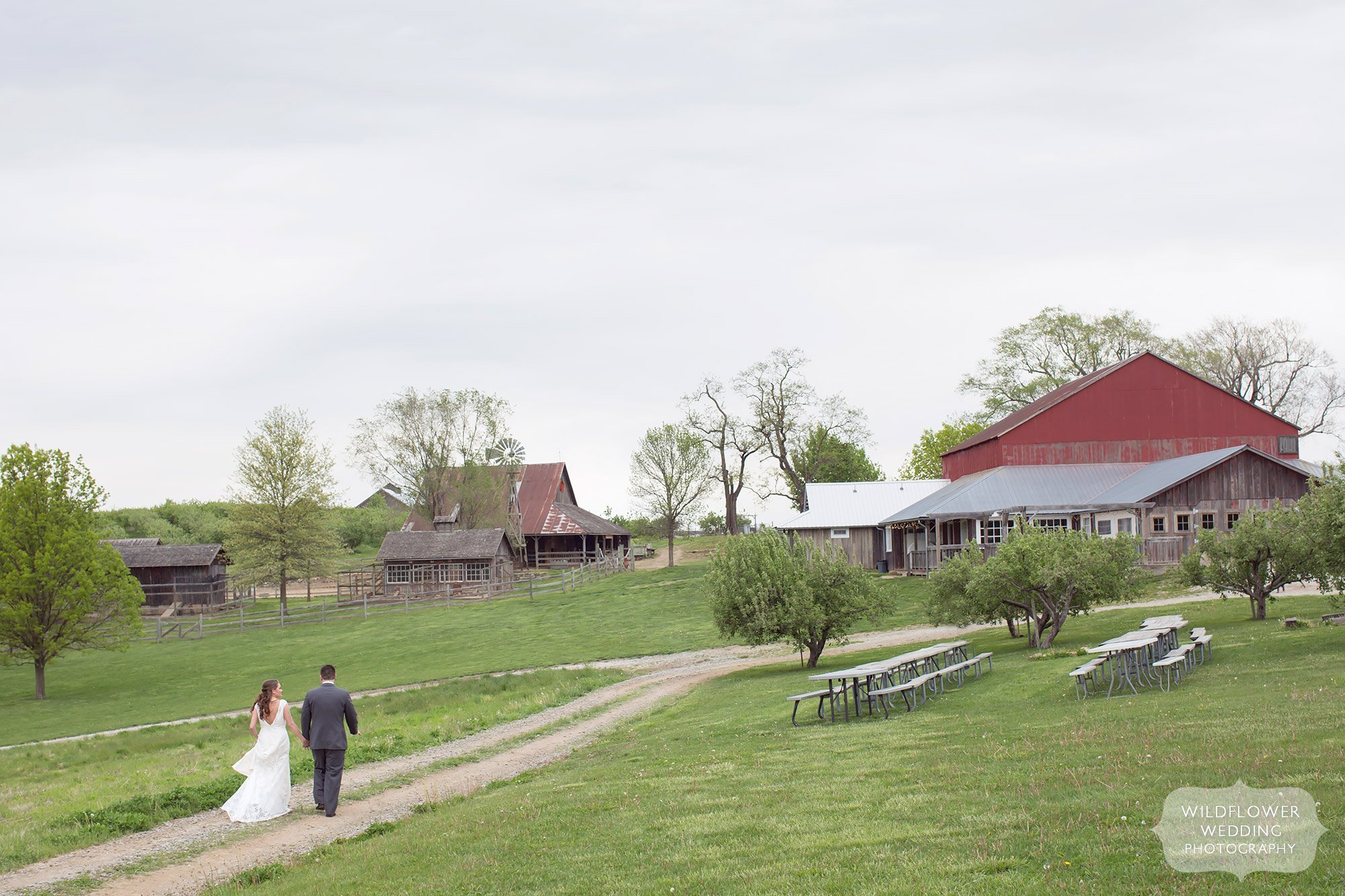 The bride and groom walk along the path at their Kansas City farm wedding at the Weston Red Barn.