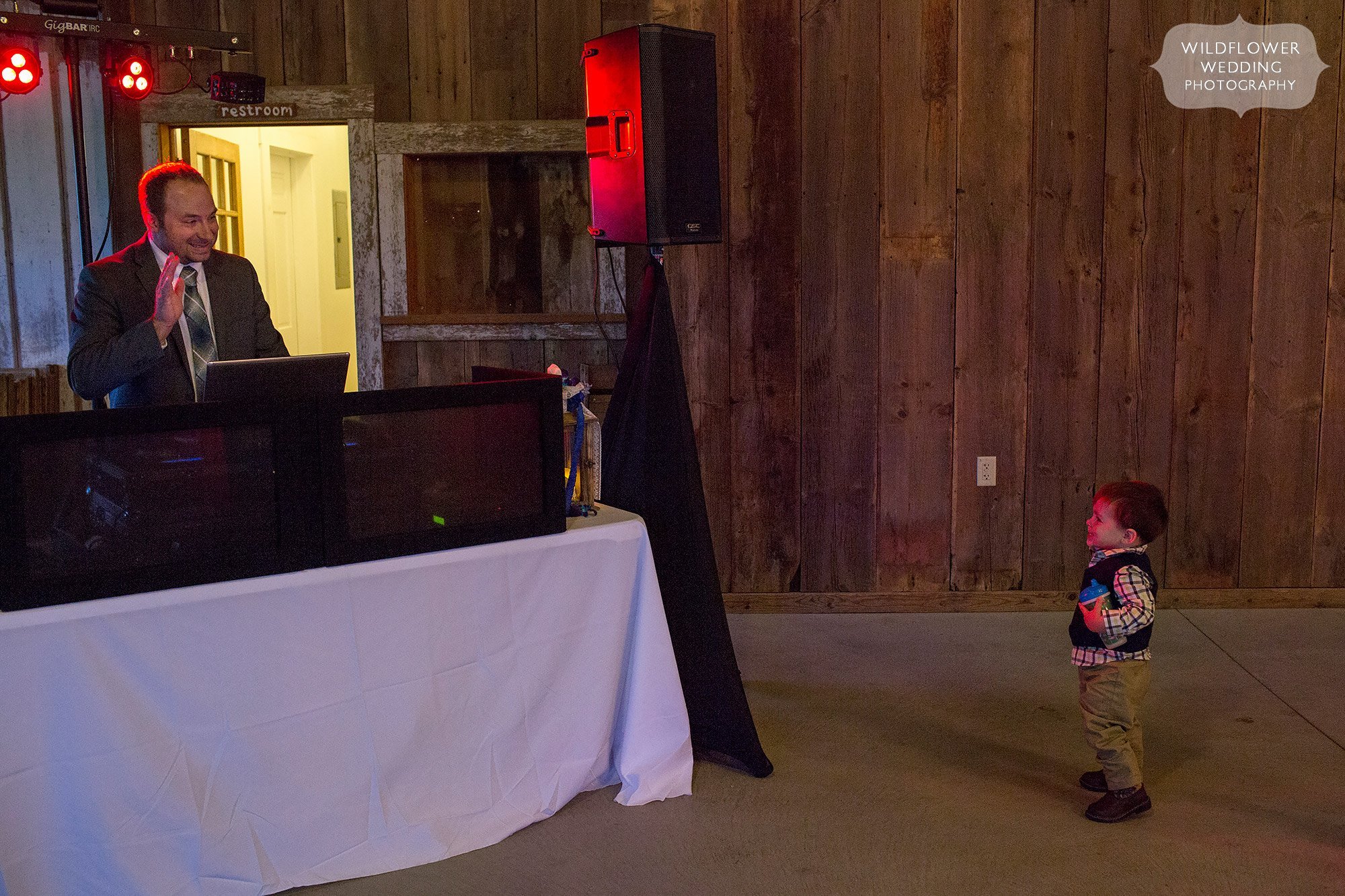 Hilarious photo of the DJ waving to a funny toddler on the dance floor at this Weston barn wedding.