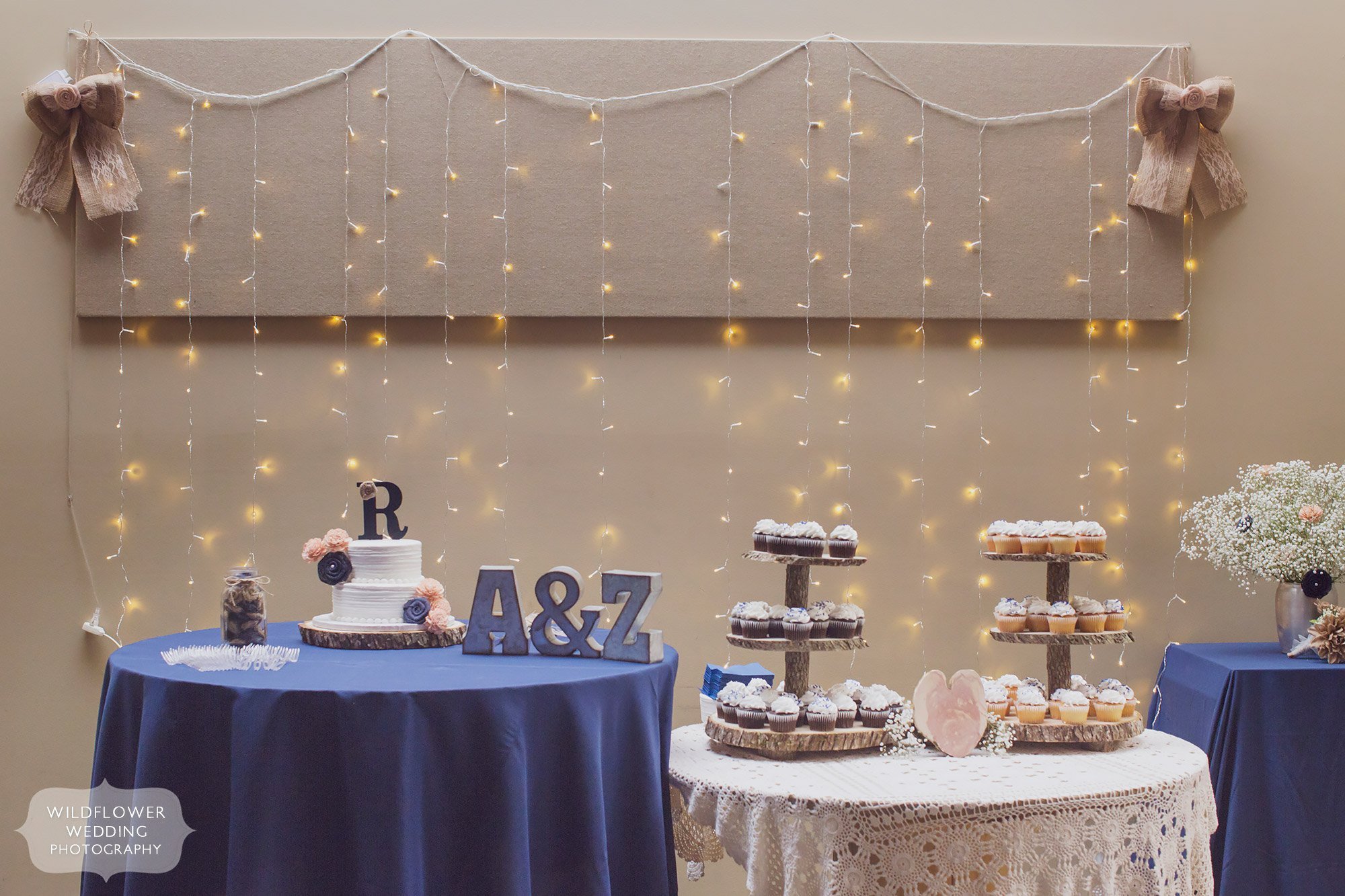 Twinkle lights hang behind this country wedding dessert table with cupcakes and a rustic wooden stand.