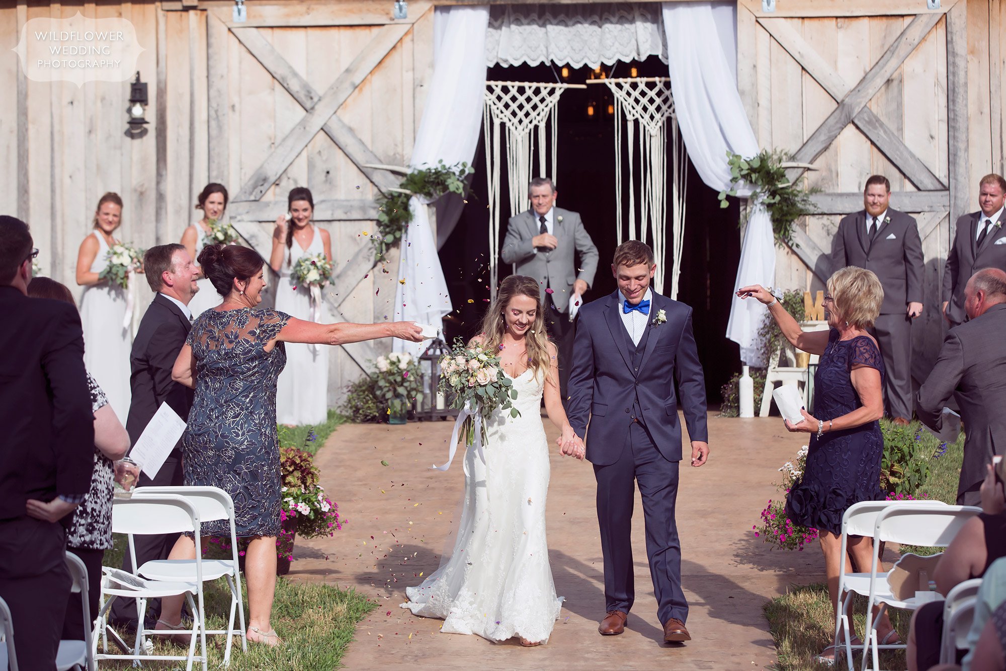 The bride and groom have a colorful wedding ceremony exit walk as the guests throw dried wildflower petals at them at this barn wedding.