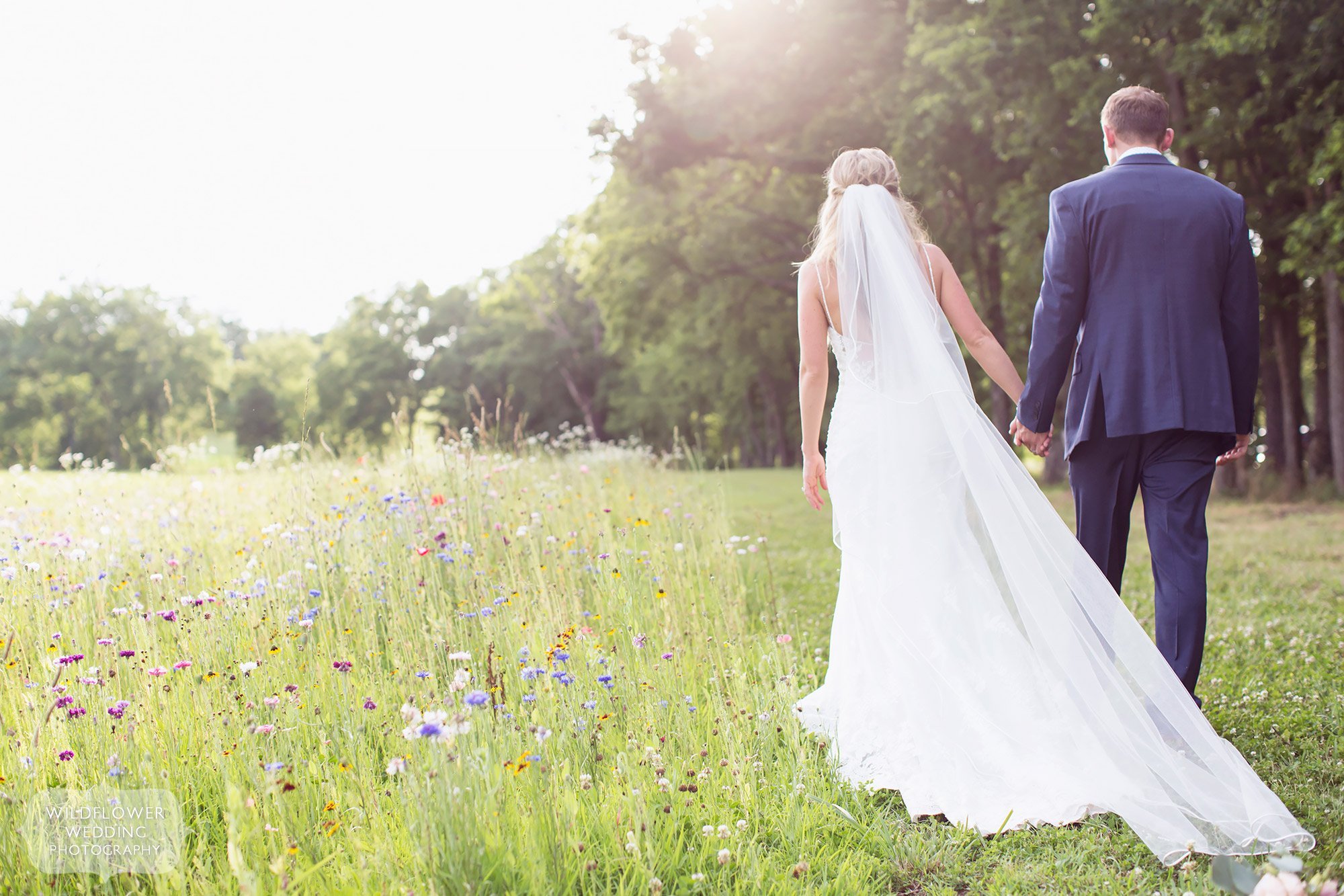 Romantic ethereal wedding photo of the bride and groom walking through a field of wildflowers at Kempker's Back 40 barn wedding venue.