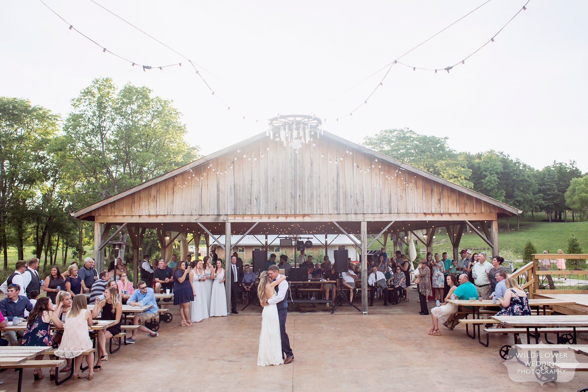 The bride and groom have their first dance outside under a canopy of twinkle lights at this barn wedding venue in Westphalia, MO.