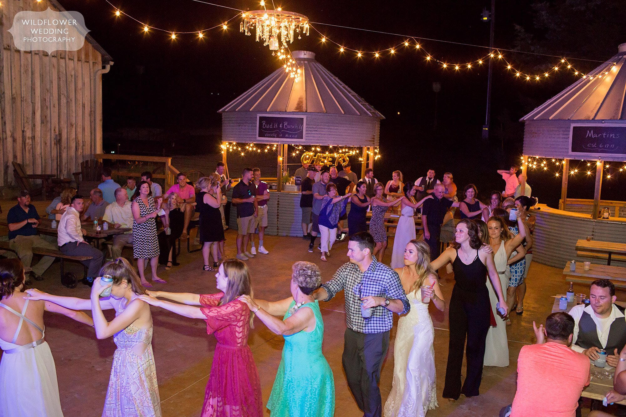 Wedding guests form a conga line on the outdoor dance patio at this barn venue in MO.
