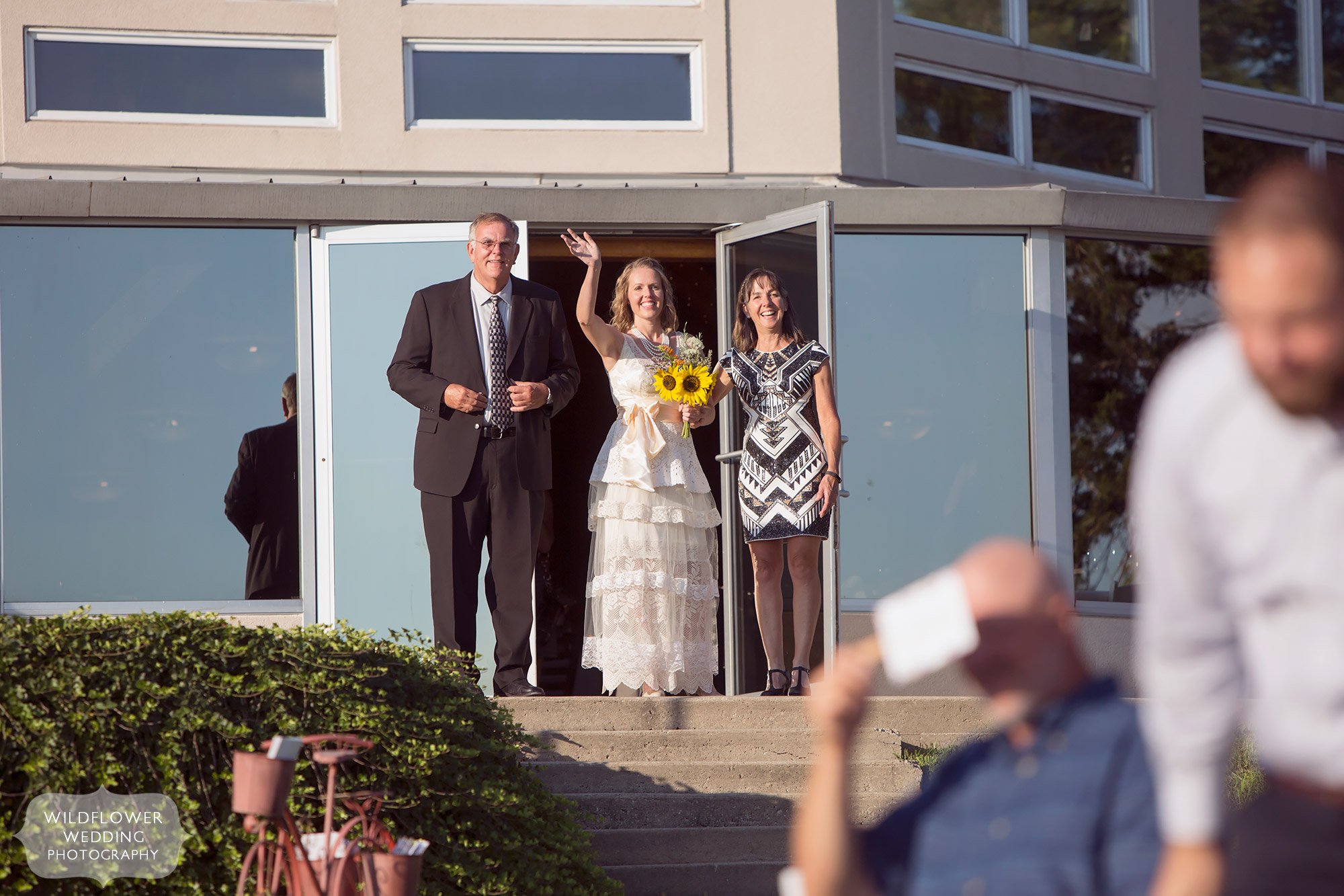 bride waving at wedding guests with parents standing on either side of her