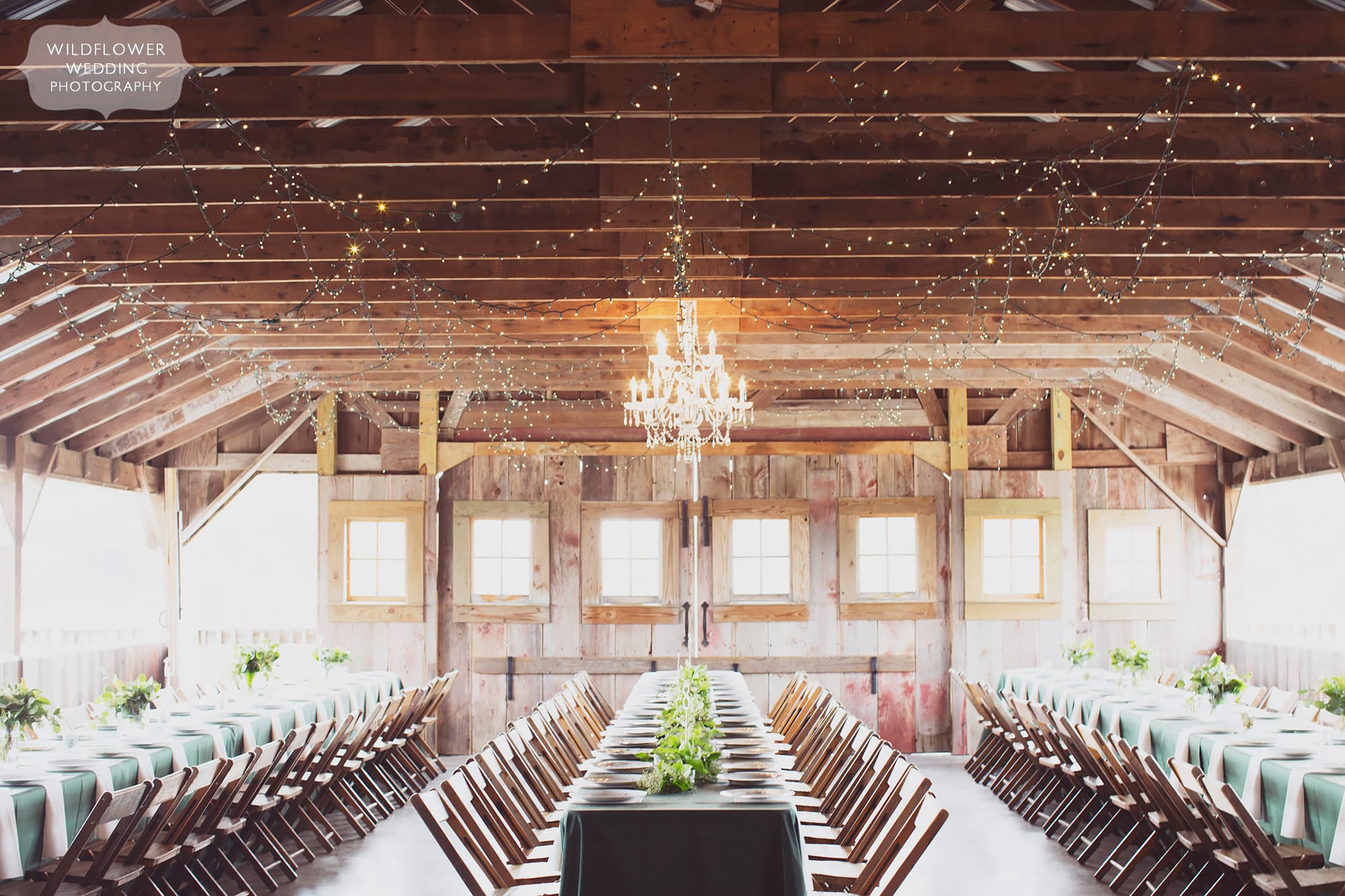 Long dinner tables are set with green tablecloths for this romantic Missouri barn wedding.