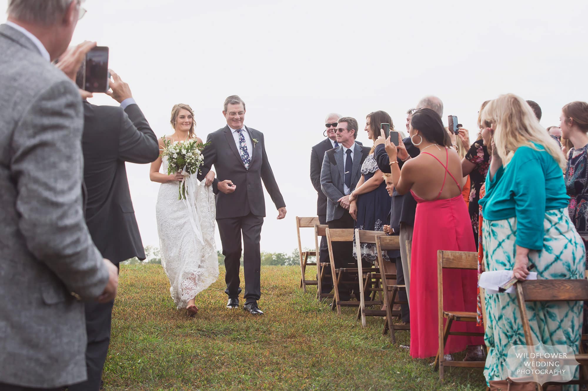 The bride and her father walk down the aisle at this outdoor Missouri barn wedding ceremony.
