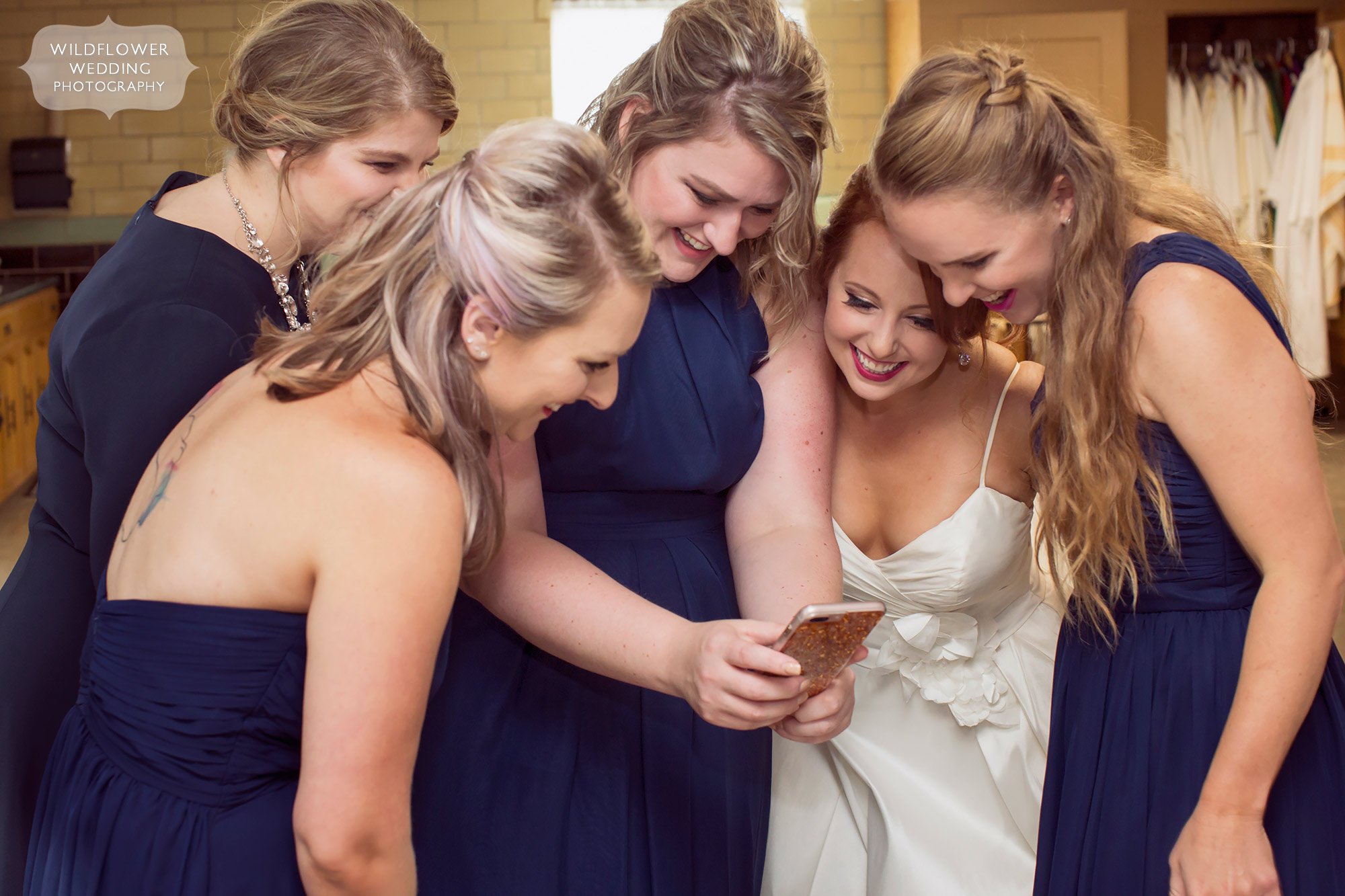 Bridesmaids all crowding around a phone to see a photo at this mid-MO wedding.