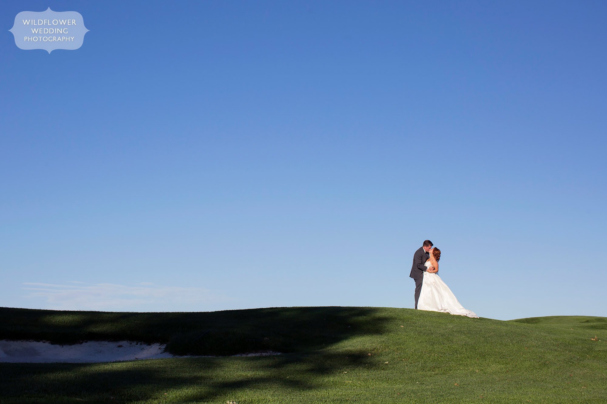 The bride and groom stand on a green hill against a blue sky at this Jefferson City Country Club wedding in MO.
