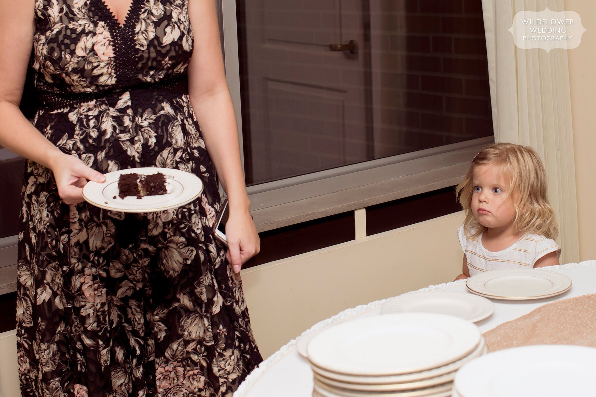 Funny documentary wedding photo of the flower girl looking at cake.