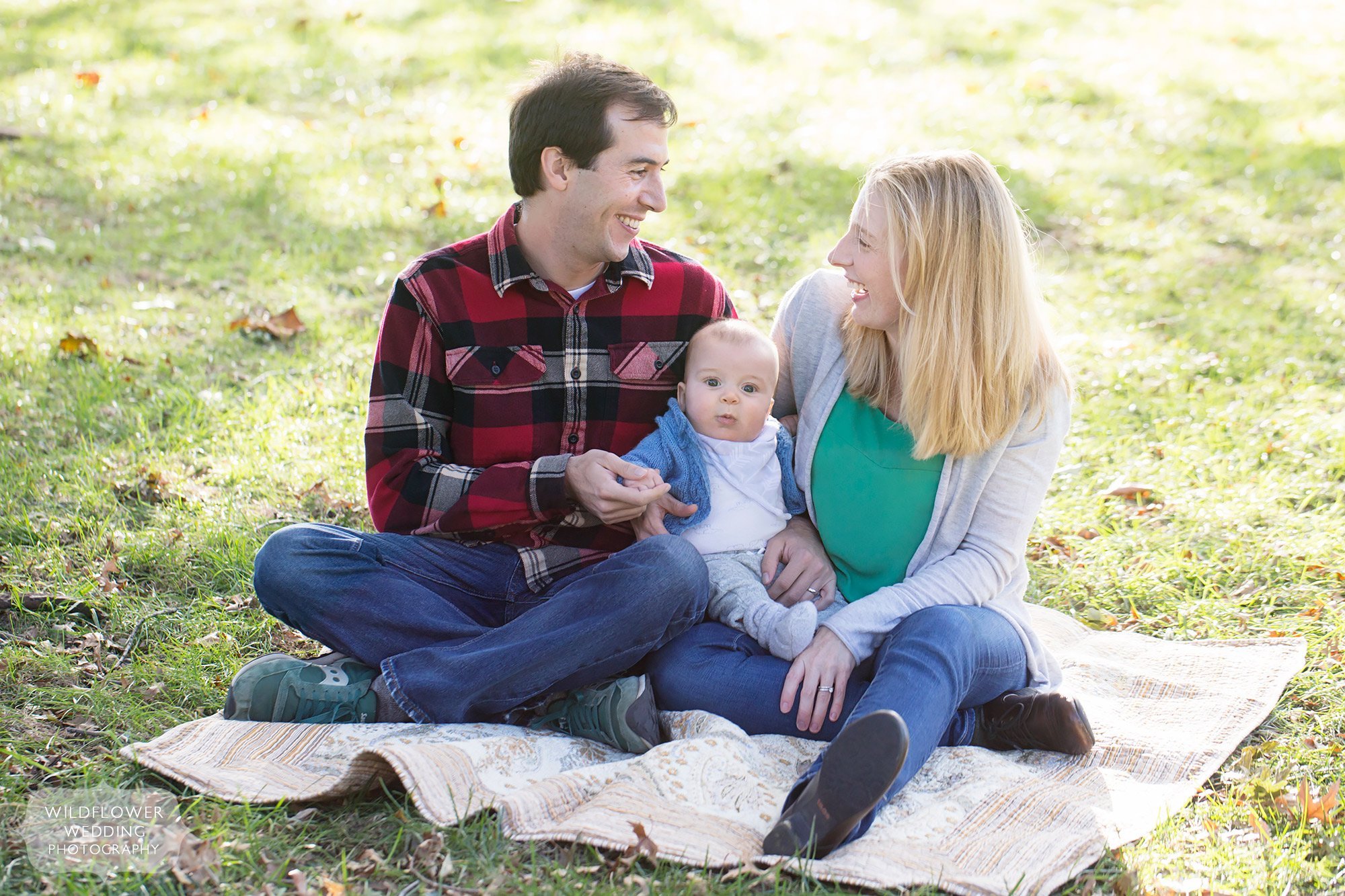Parents and their baby sit on a quilt in Loose Park for a family photo session in the fall.