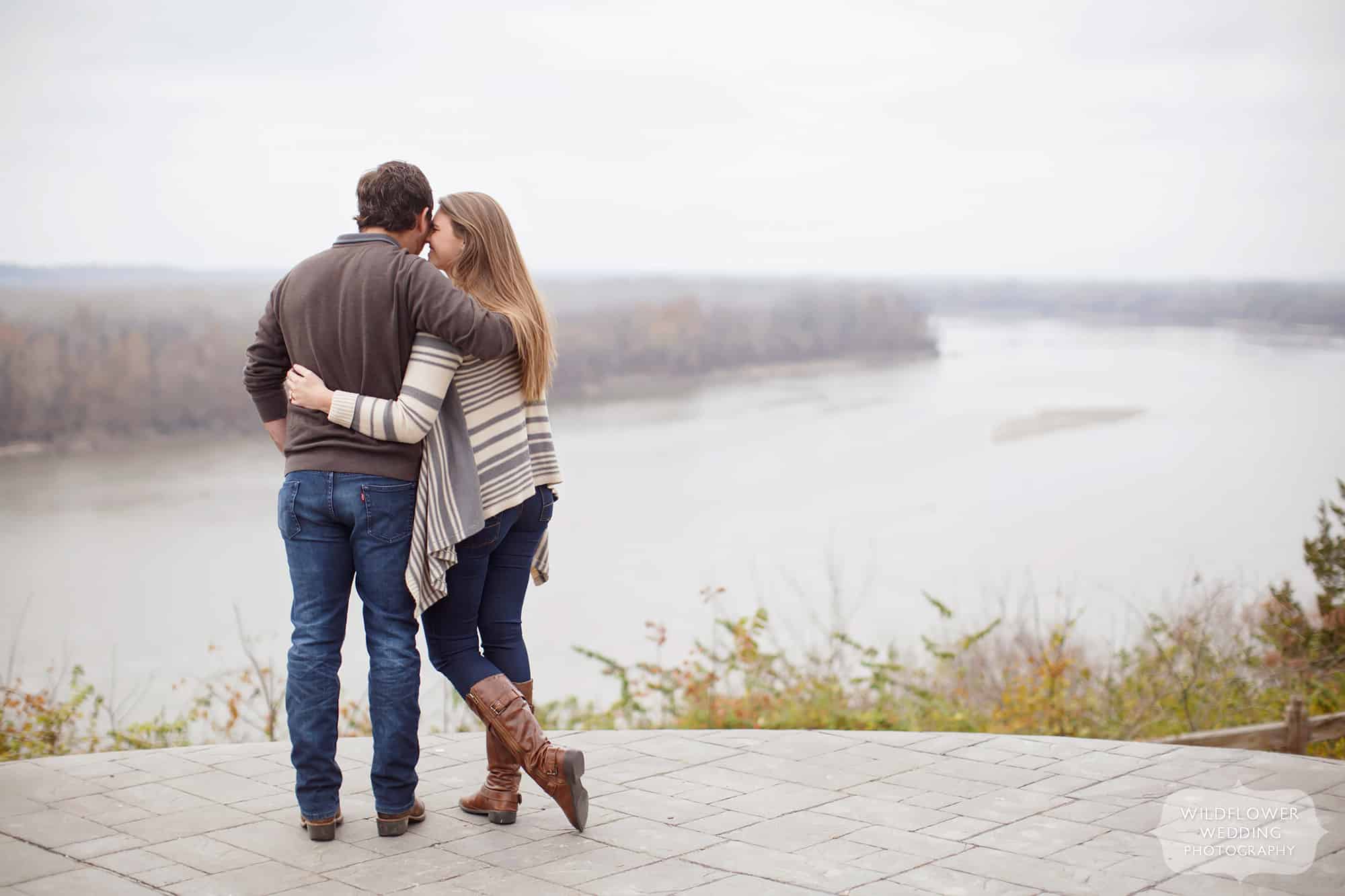 The newly engaged couple stands at the edge of the blufftop overlooking the Missouri River after a surprise wedding proposal photography shoot.