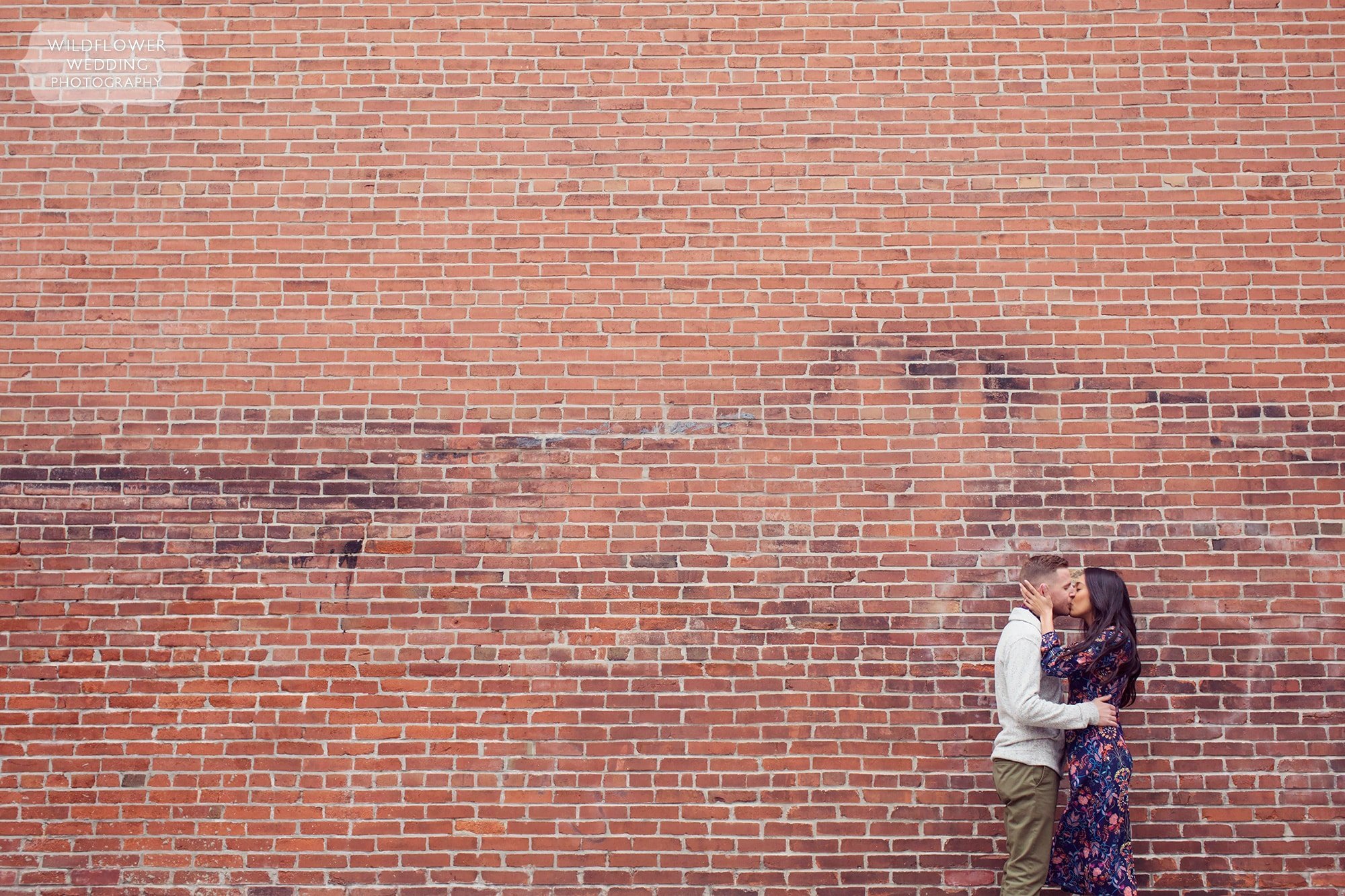 Engaged couple kisses in front of giant brick wall in Columbia, MO.