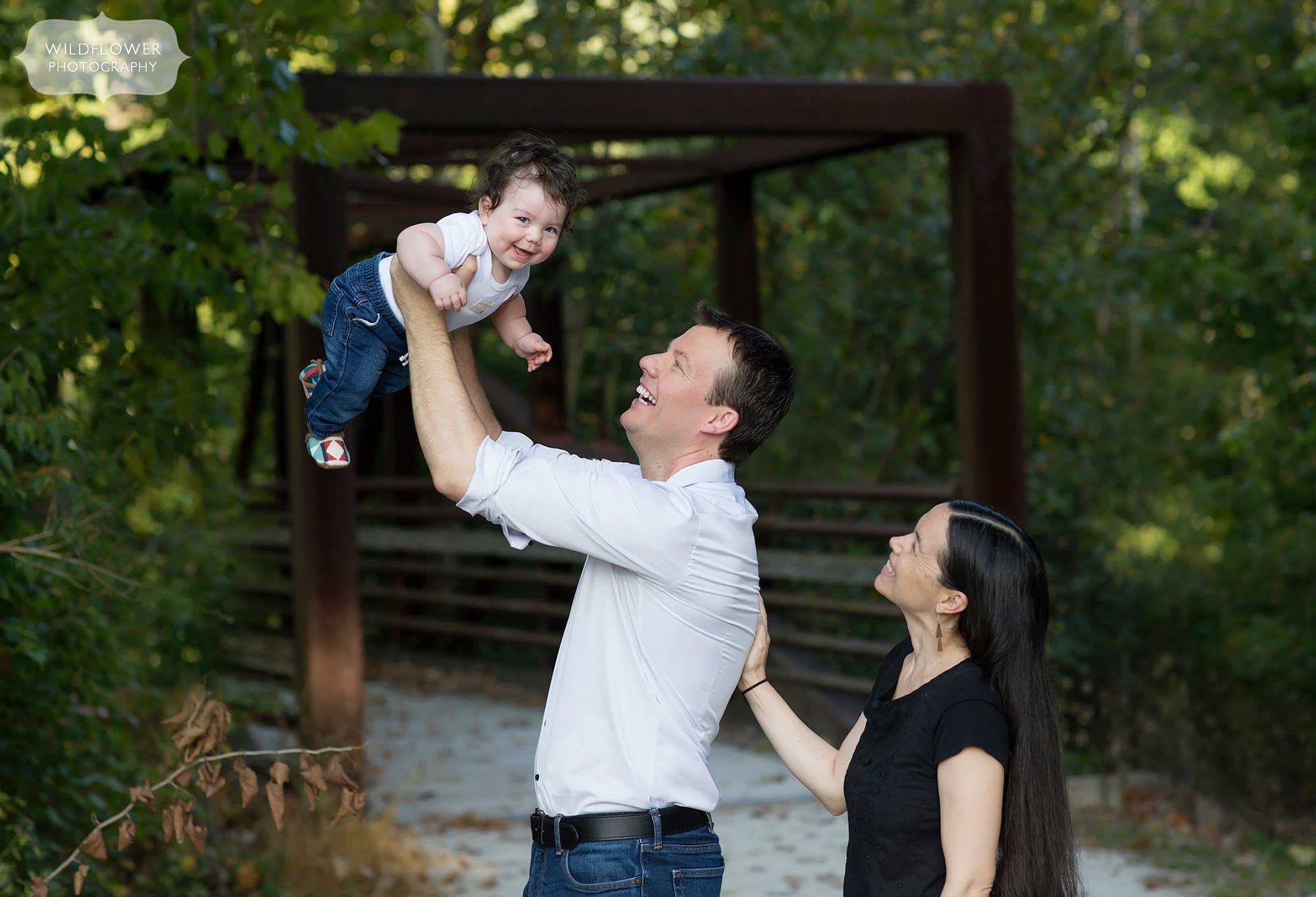 Happy family photography with dad holding baby up in the air at MKT bridge in Columbia, MO.