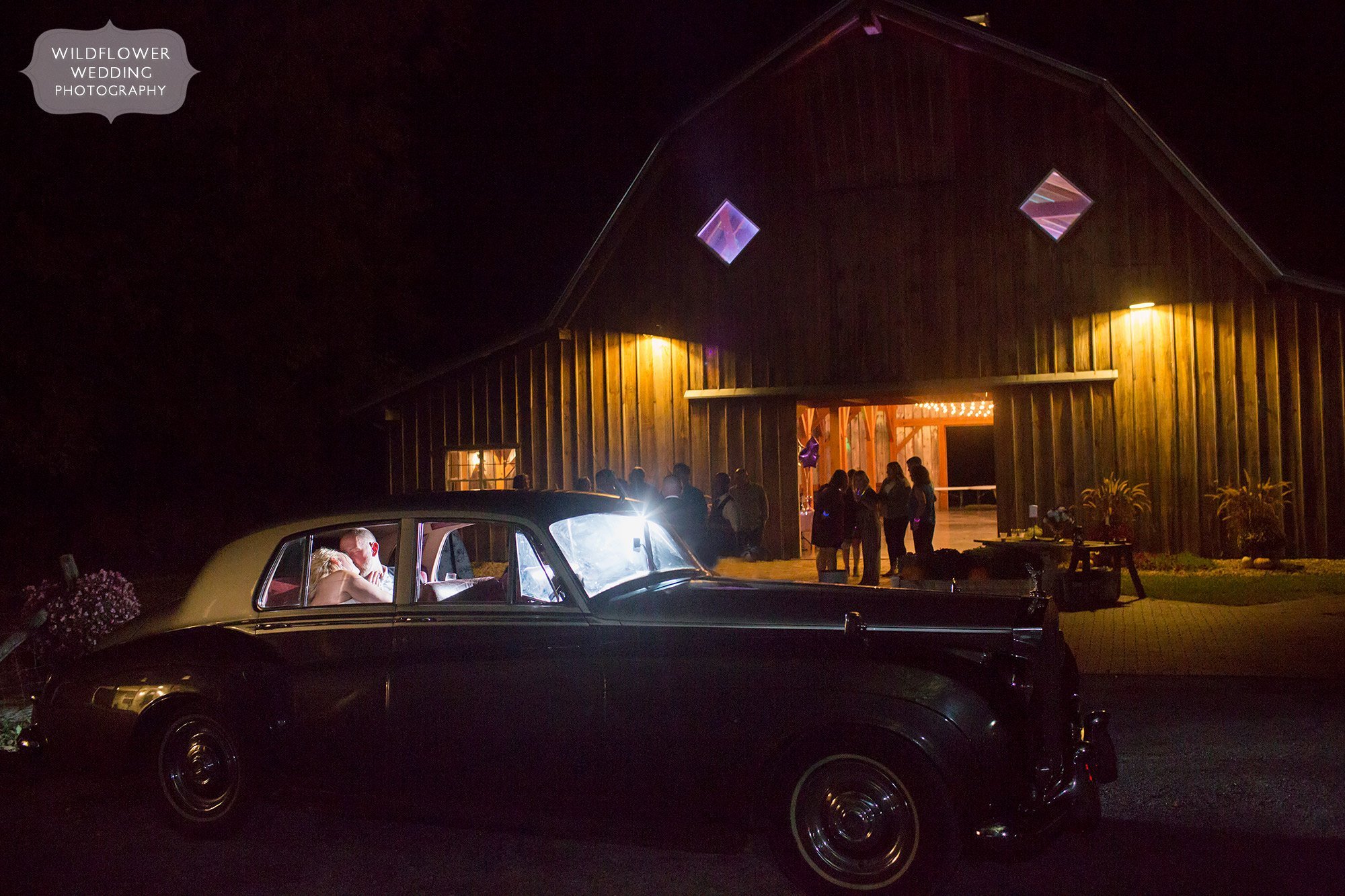The bride and groom kiss in the back of their Rolls Royce at night for KS barn wedding.