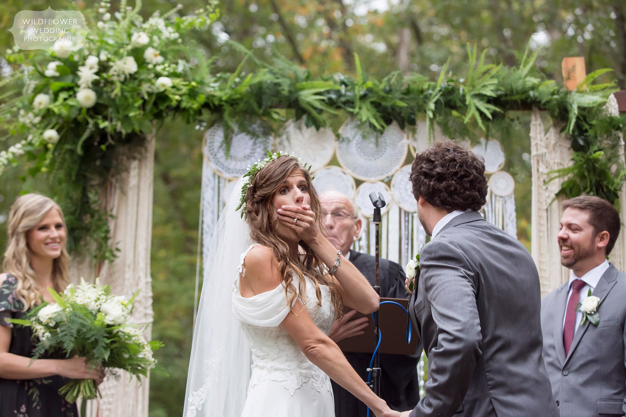 Documentary wedding photo of the bride with her hand over her mouth, shocked during Little Piney Lodge wedding.