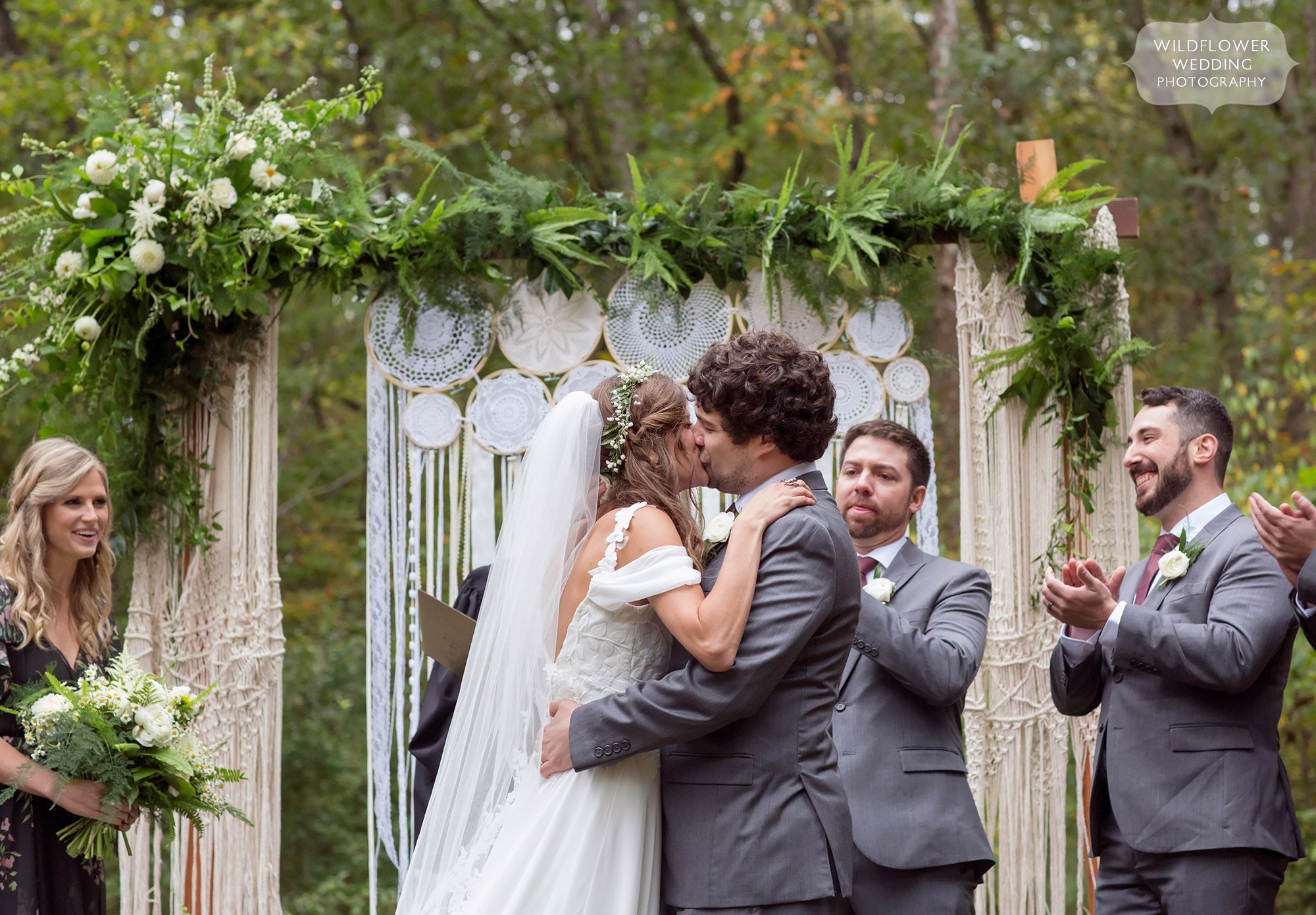 The bride and groom kiss at the end of their outdoor wedding ceremony at Little Piney Lodge.