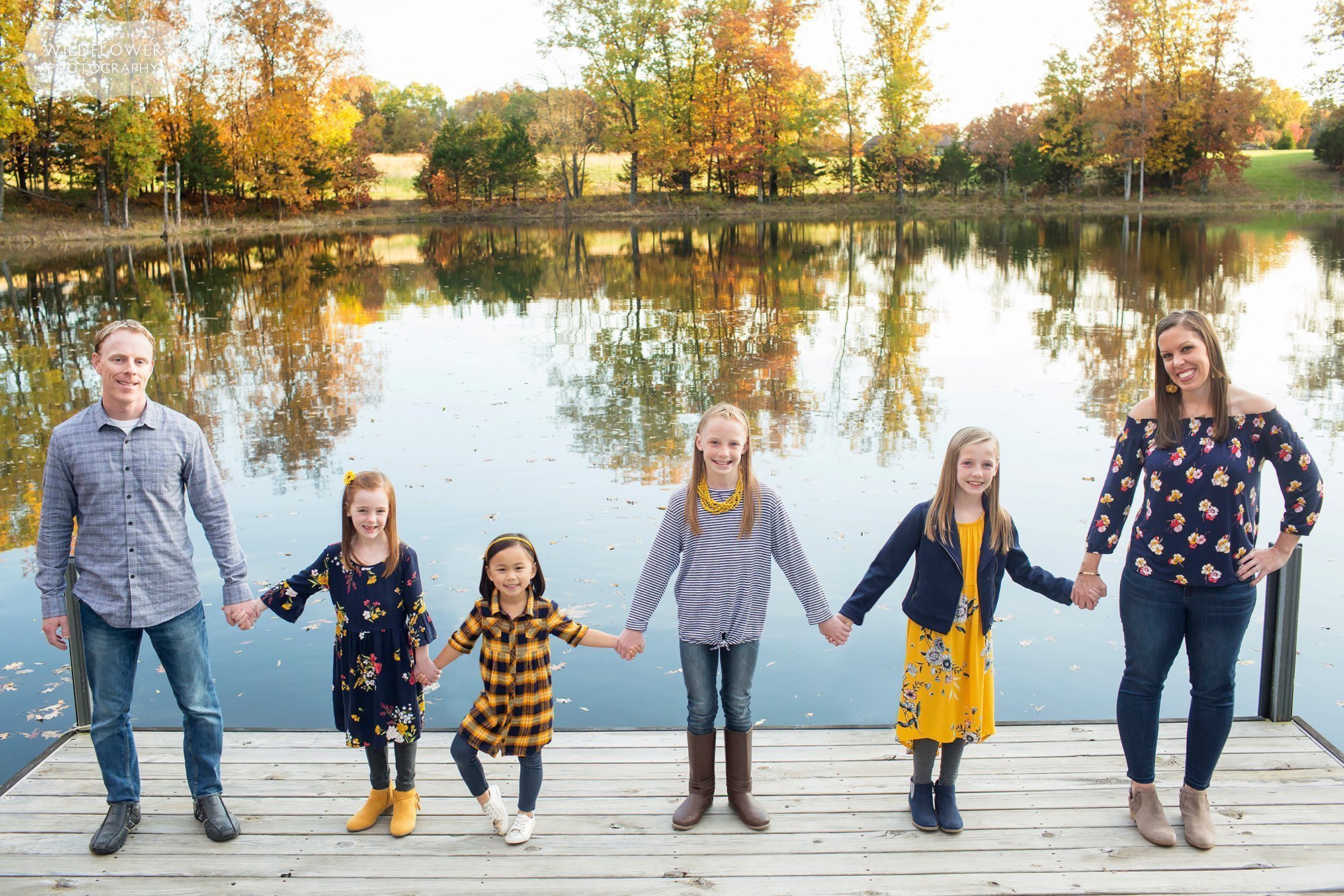 These fall family pictures in Columbia, MO have family line up on a dock with lake behind them.