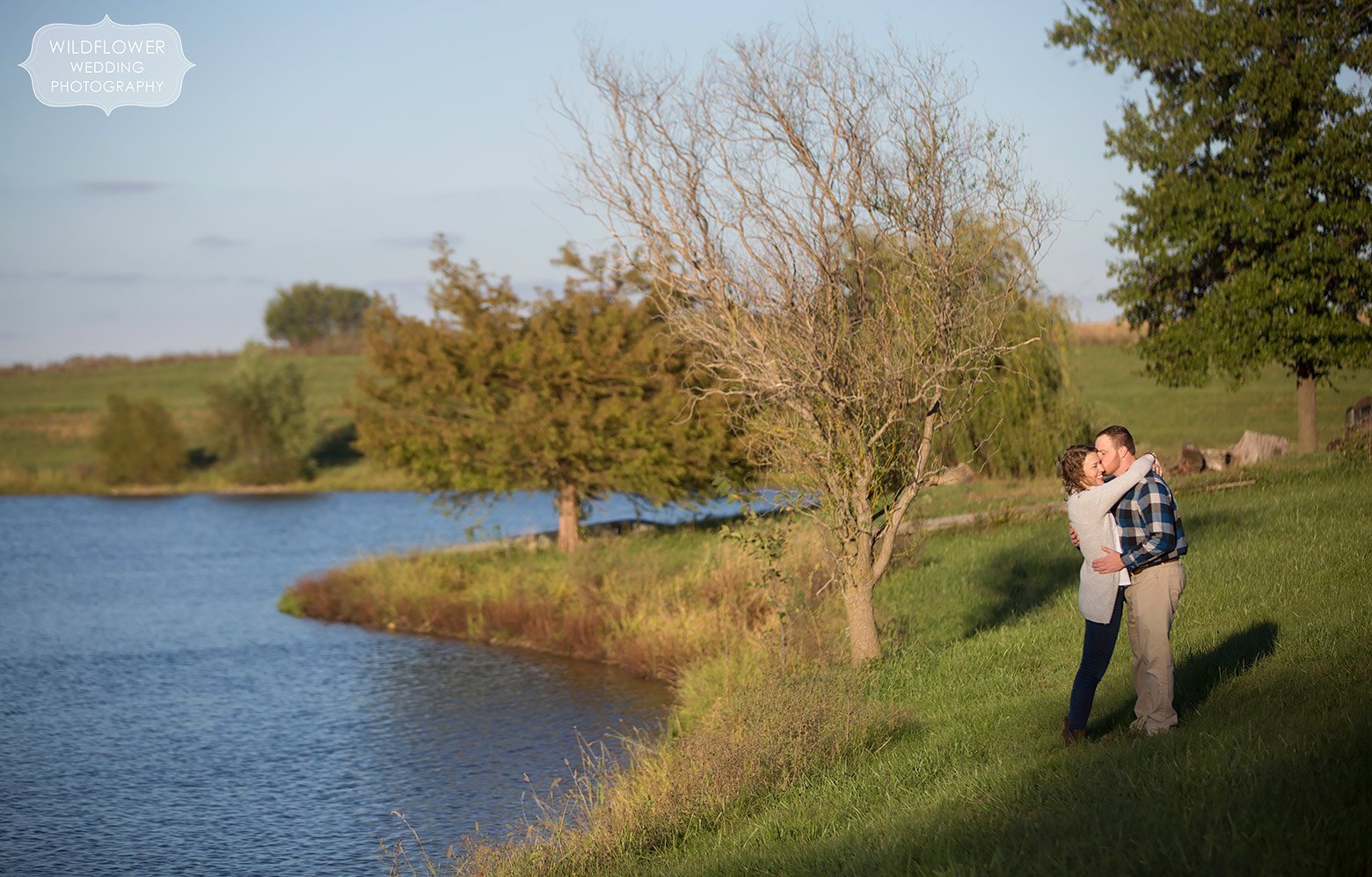 Couple stands by a pond during their country engagement session at a family farm Boonville, MO.