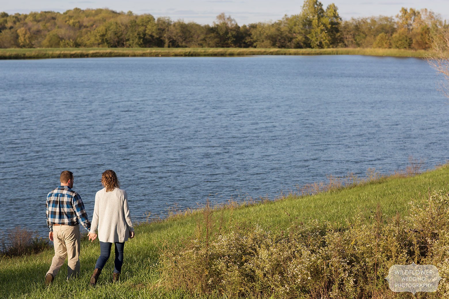 Couple holds hands while walking around the pond at this Boonville, MO engagement session.