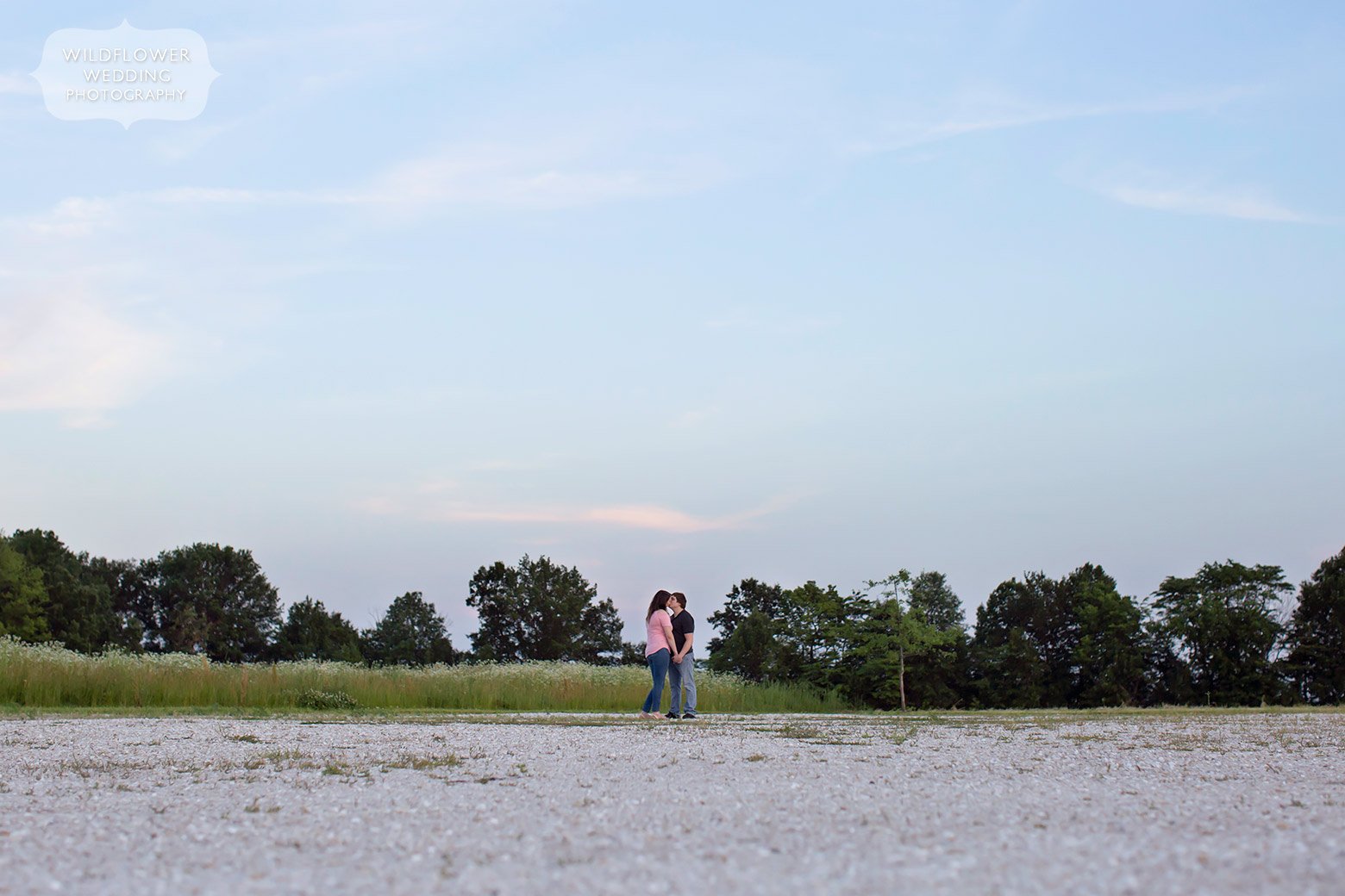 Couple stands under big sky in landscape engagement photo at Emerson Fields.