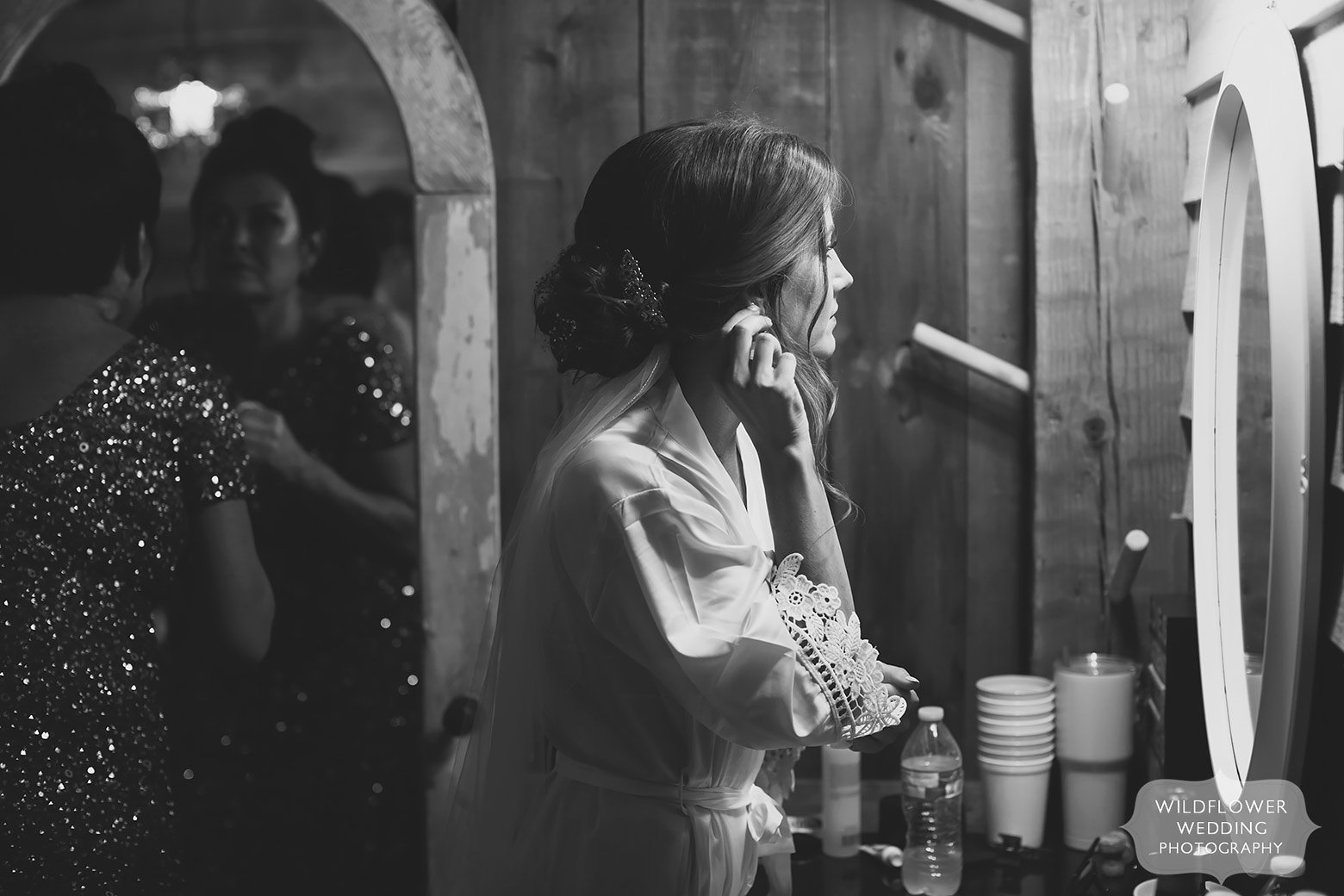 Bride looks in a mirror to fix her earring at the Weathered Wisdom Barn.